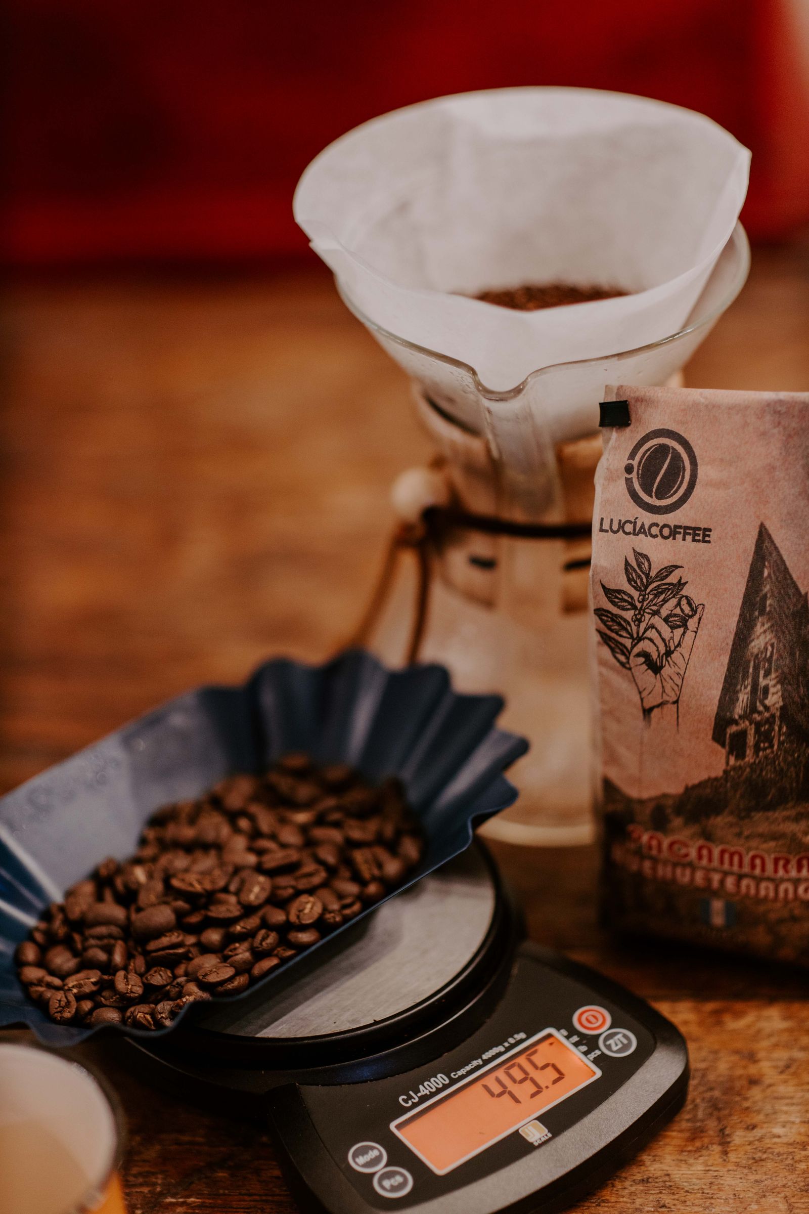 Coffee beans on a digital kitchen scale beside a pour-over dripper and a bag of beans