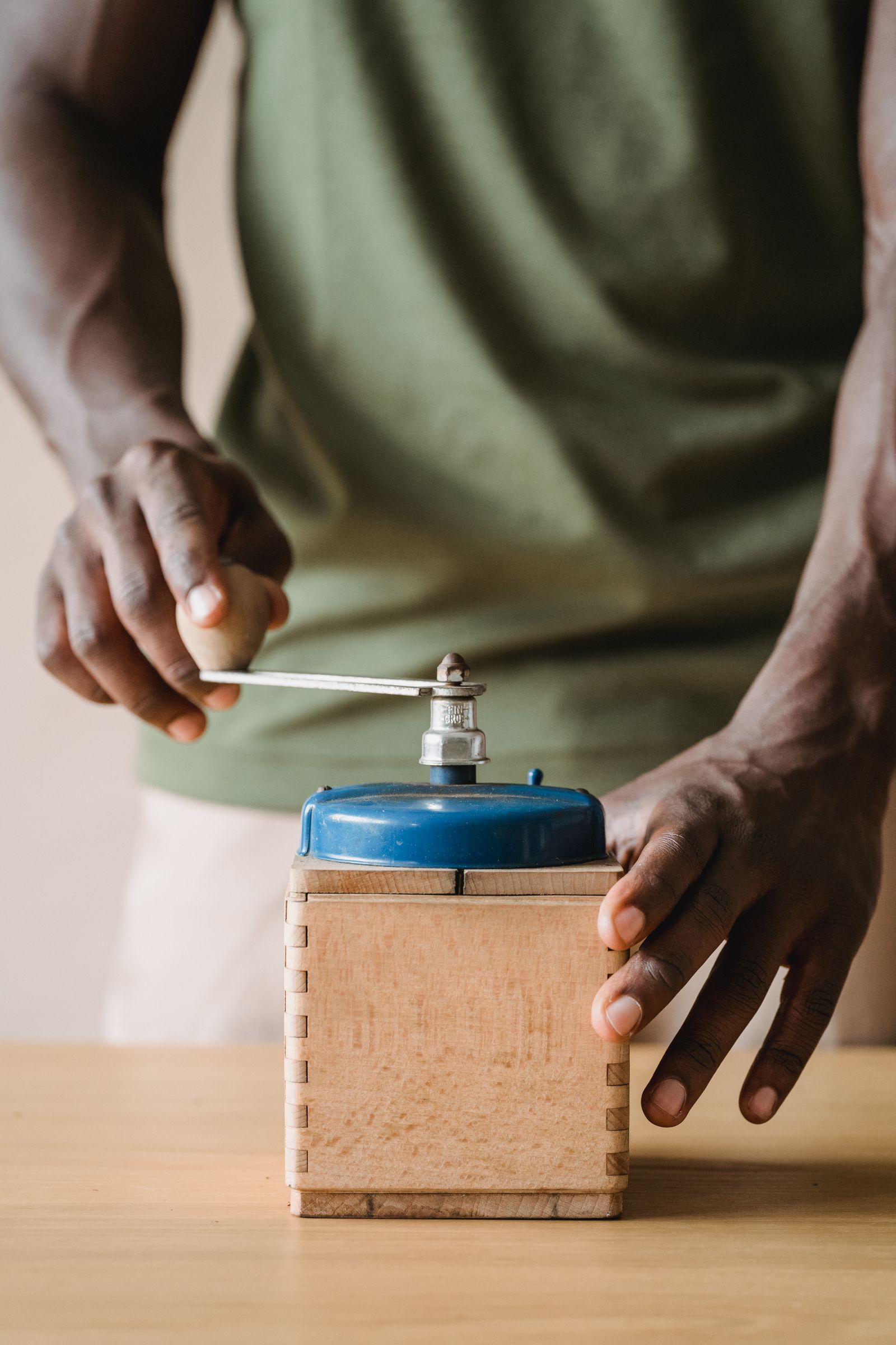 A person grinding coffee beans by hand with a manual burr grinder on a wooden counter