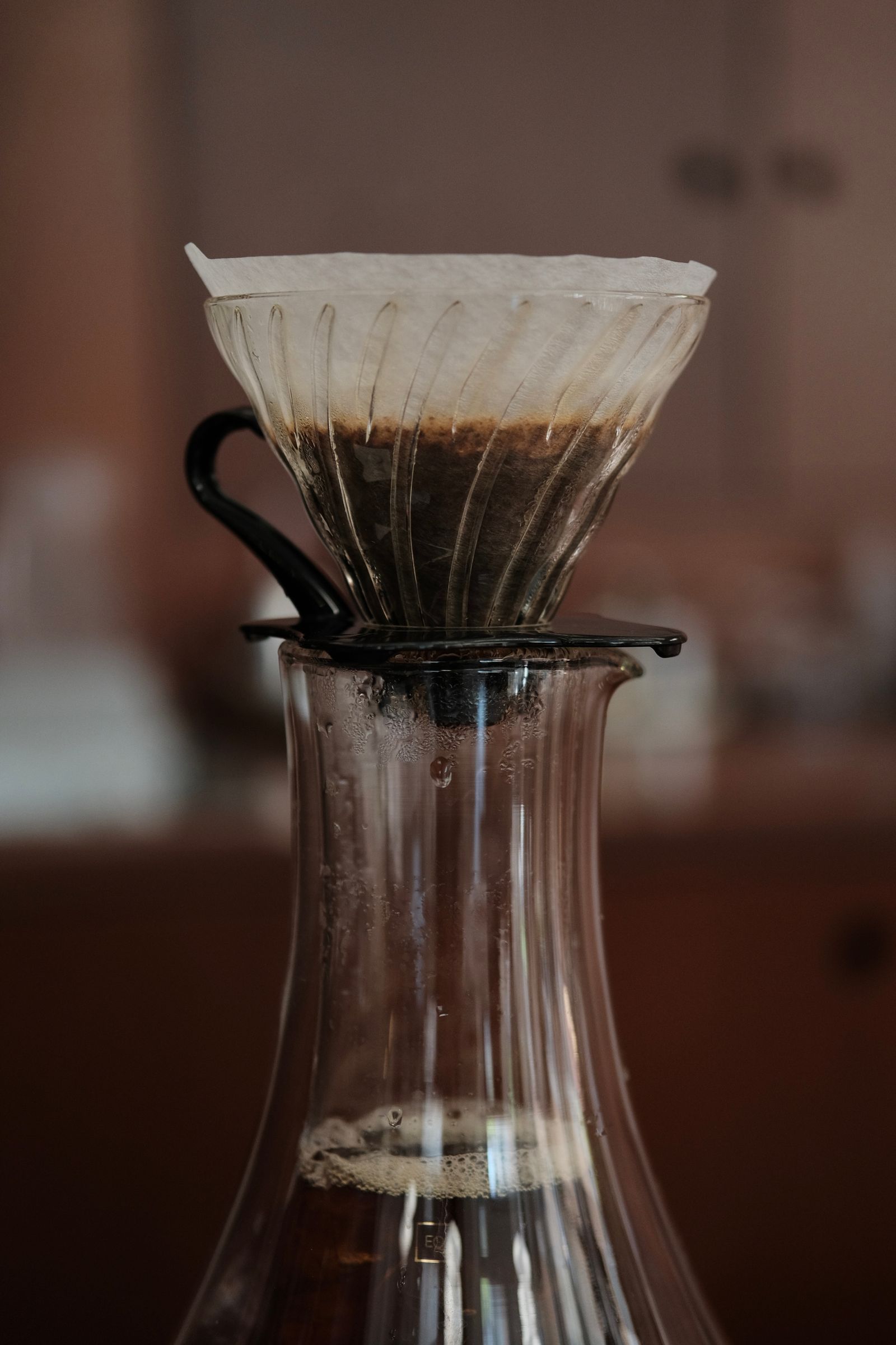 A white paper cone filter seated in a glass pour-over dripper, mid-brew over a glass server