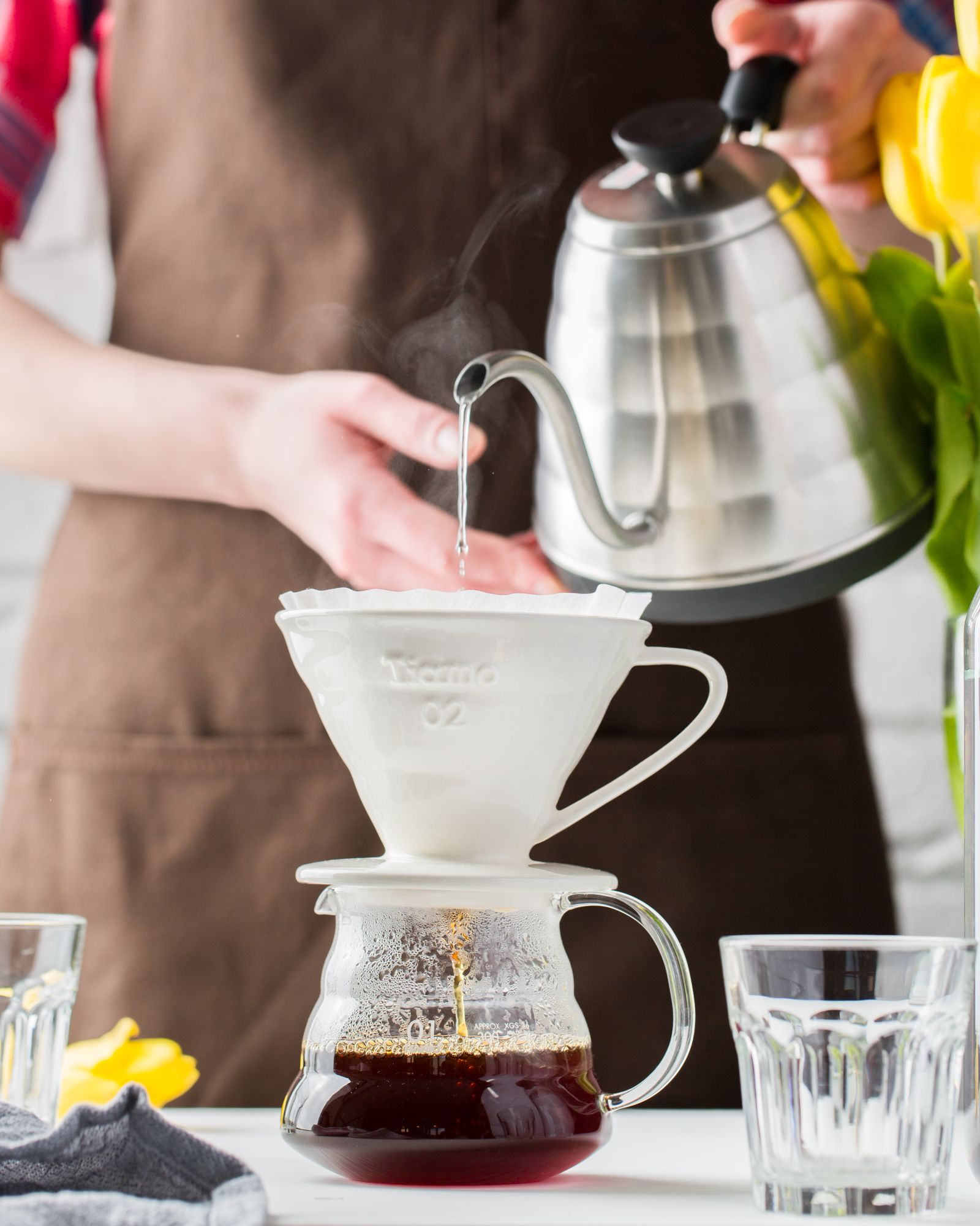 Pouring hot water from a gooseneck kettle over a V60 dripper into a glass carafe