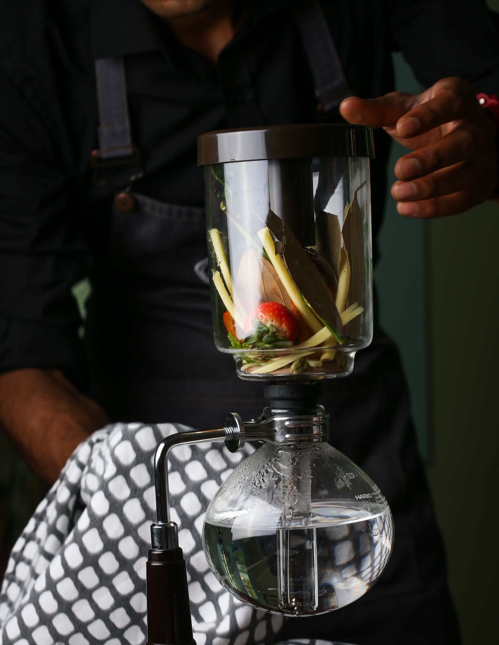 A glass hot-infusion siphon brewing over an open flame