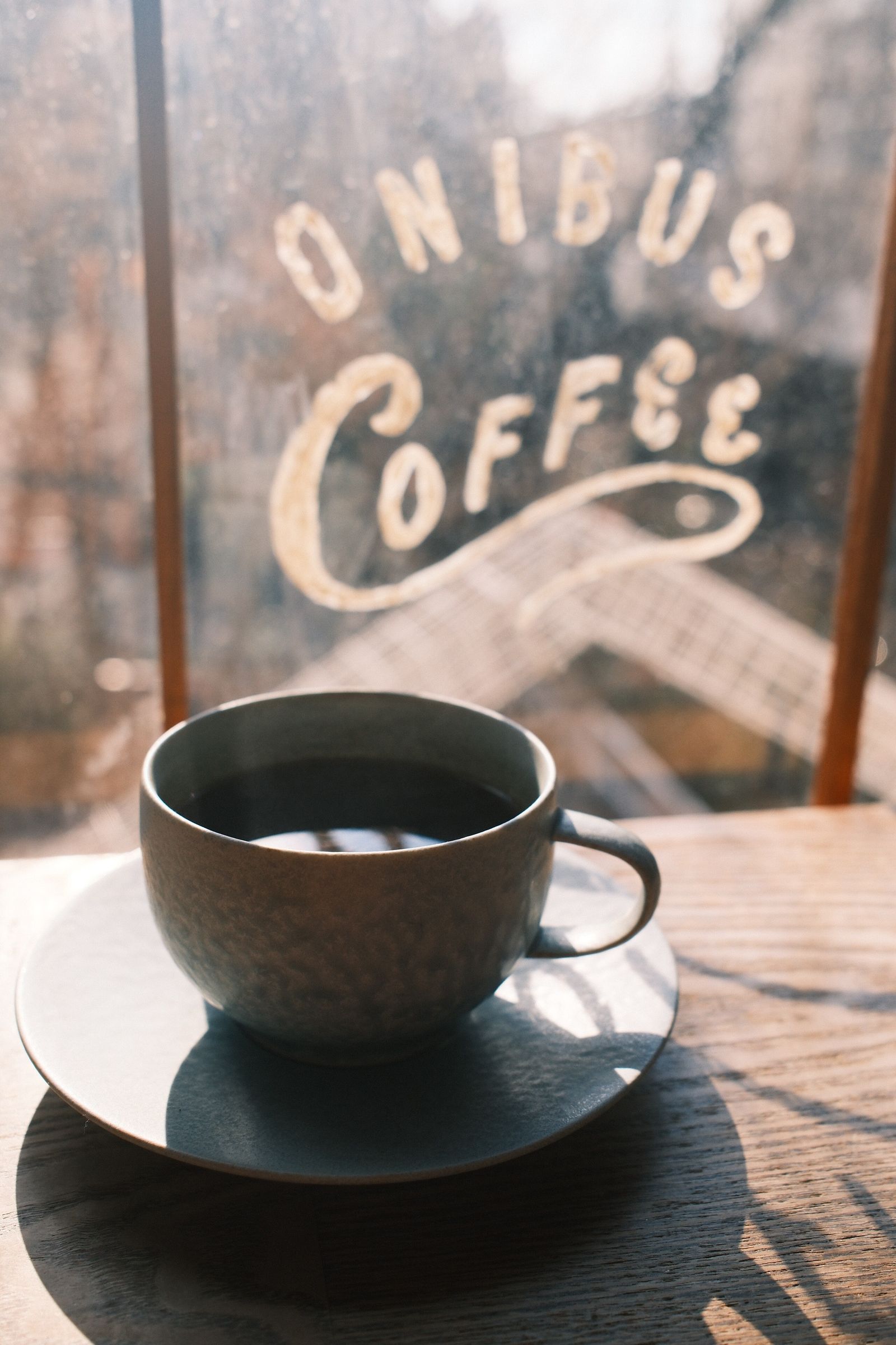 A cup of black coffee on a saucer by the window of a Tokyo coffee shop, with hand-lettered signage on the glass