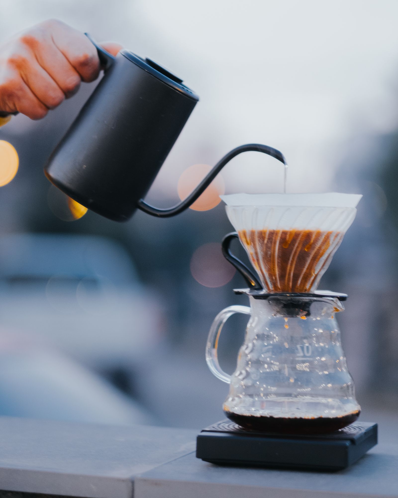 A barista pouring a slow, thin stream of hot water over a Hario V60 dripper