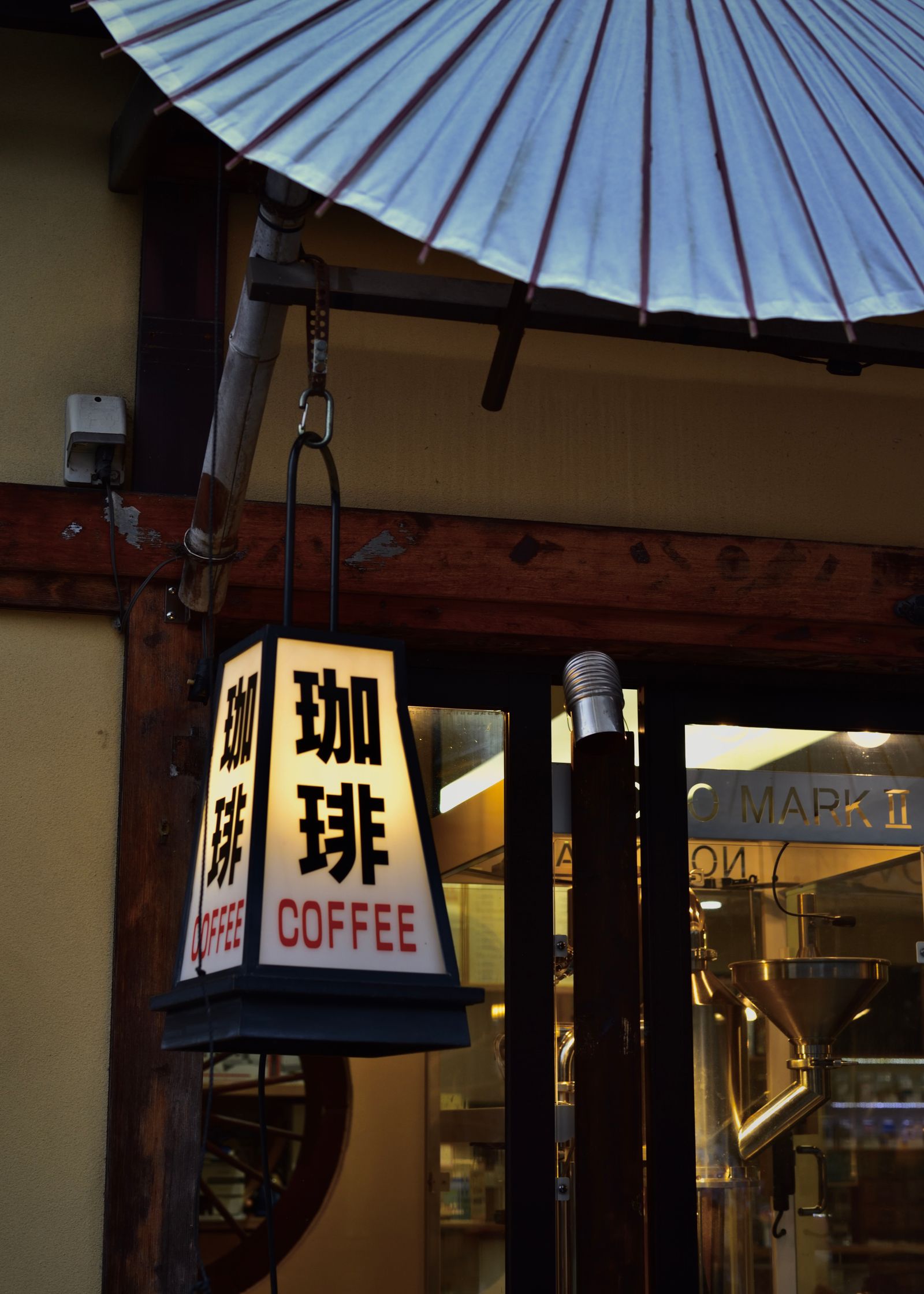 Traditional Japanese coffee shop storefront with an illuminated 珈琲 (coffee) lantern and a paper parasol