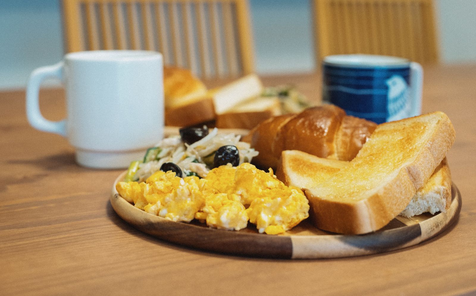 A kissaten-style plate of thick-cut buttered toast, scrambled eggs and a sandwich, served with coffee on a wooden table